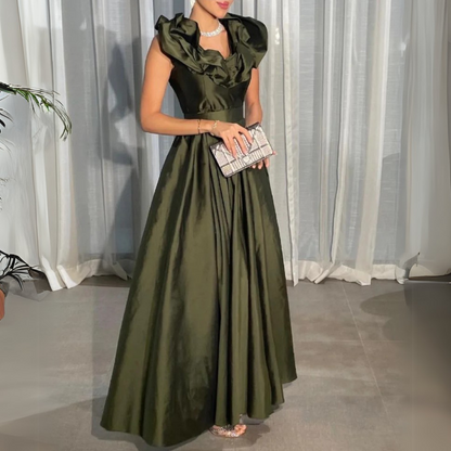 A woman wearing a green, satin, floor-length evening dress with short puffed sleeves and an off-shoulder neckline, holding a clutch and wearing open-toe heels.