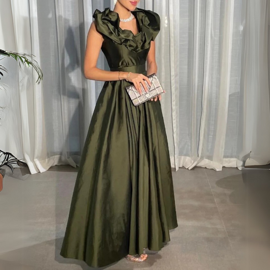 A woman wearing a green, satin, floor-length evening dress with short puffed sleeves and an off-shoulder neckline, holding a clutch and wearing open-toe heels.